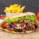 Döner Kebab Doner Kebap fast food in flatbread with fries on a wooden board