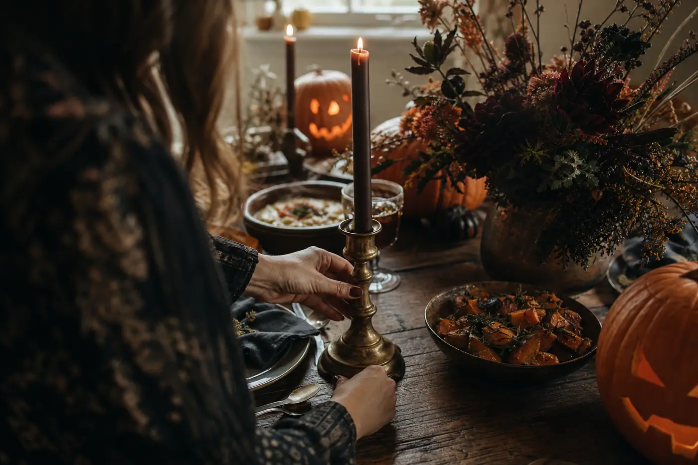 Halloween Dinner Ideas: Plan a Spooky & Stress-Free Party at Home Close-up of host’s hands arranging candles and dark florals on an elegant Halloween dinner table with rustic autumn dishes.